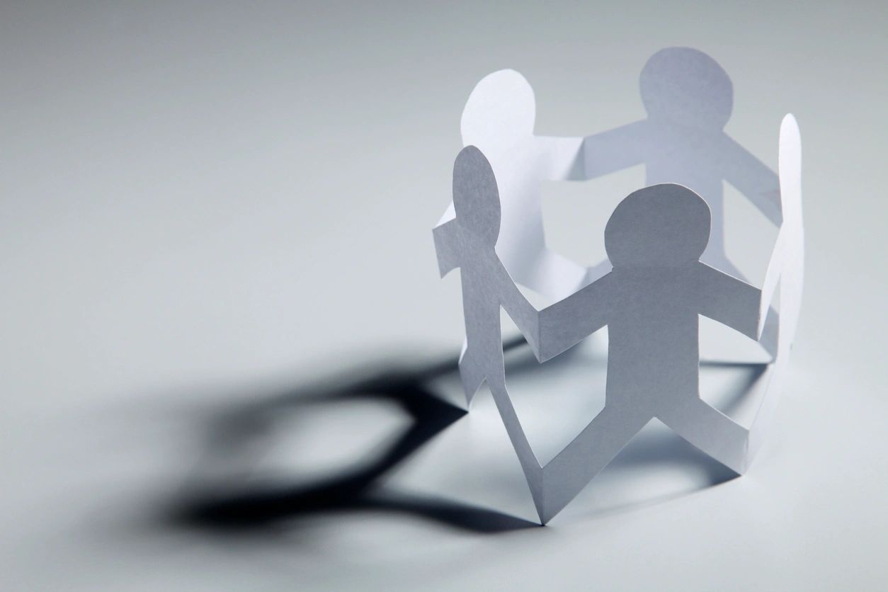 Paper chain of human figures casting shadows on a light background.